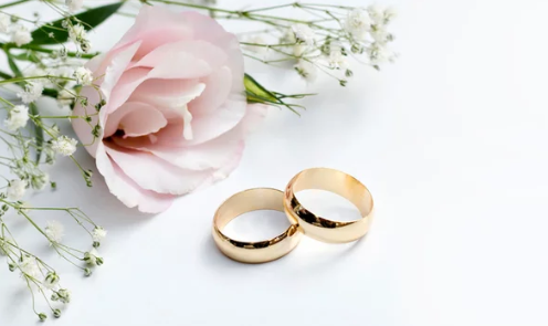 2 gouden ringen mer er naast een lichtroze roos en gipskruid erbij